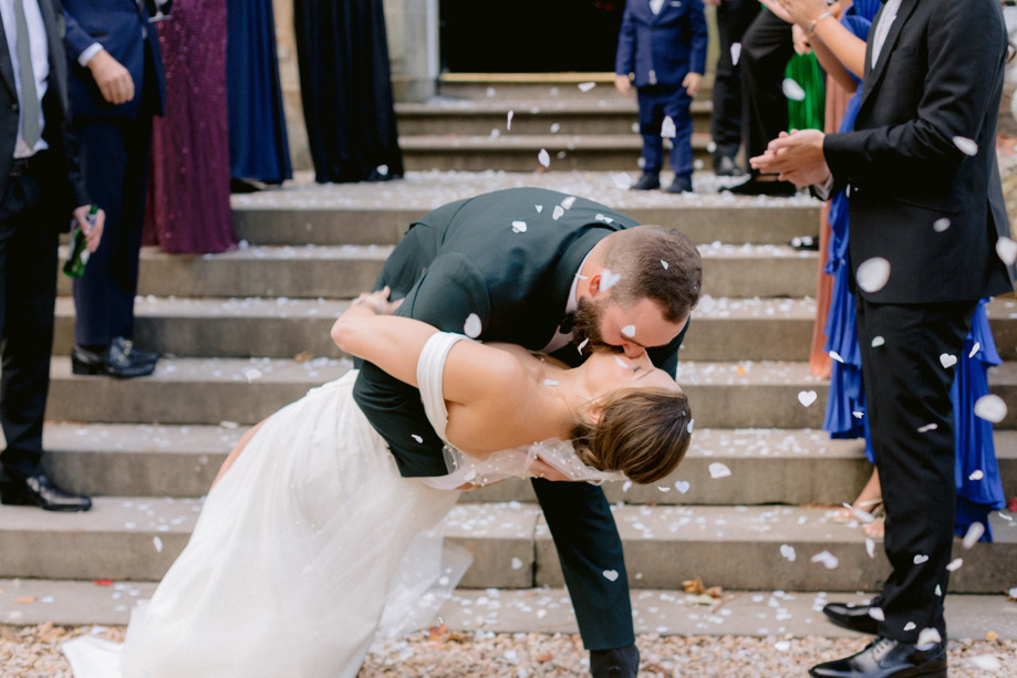 Groom dip kisses his new wife while guests throw confetti